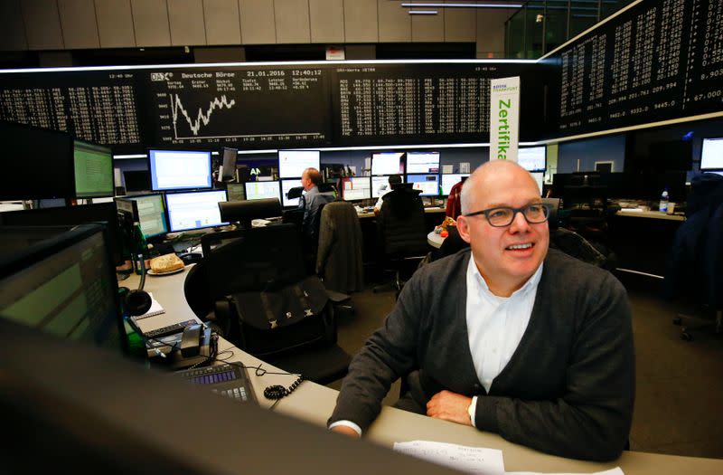 A trader works at his desk in front of the German share price index, DAX board, at the stock exchange in Frankfurt