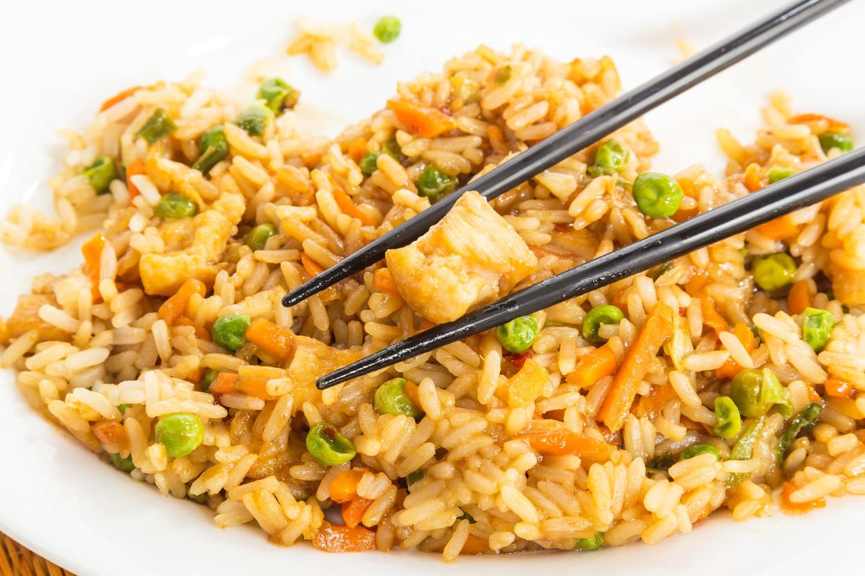 Closeup of better than takeout chicken fried rice with a pair of black chopsticks holding a piece of chicken on a white plate