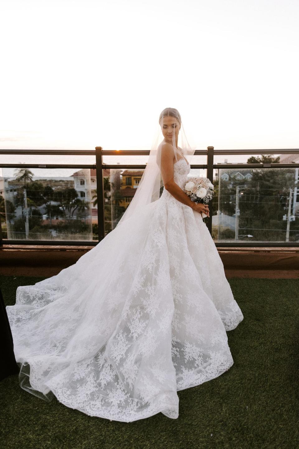 A bride stands with a veil covering her face in front of a sunset.