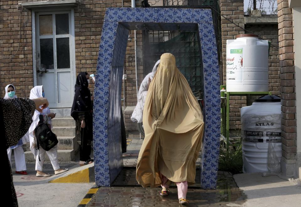 FILE - In this Monday, Sept. 14, 2020 file photo, students walk through a disinfectant tunnel as they arrive to Benazir Bhutto Women University for an examination ahead the university reopening in Peshawar, Pakistan. As coronavirus vaccines trickle into some of the poorest countries in Asia, Africa and the Middle East, data suggest some women are consistently missing out, in another illustration of how the doses are being unevenly distributed around the world. (AP Photo/Muhammad Sajjad, file)