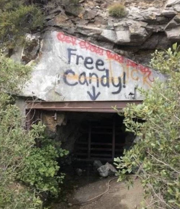 Graffiti pe o stâncă deasupra intrării unei mici peșteri scrie "Bomboane gratis" cu o săgeată îndreptată în jos