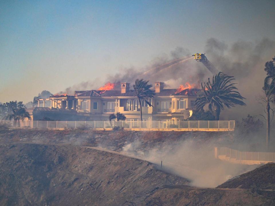 crane shoots water at burning mansion home on hill