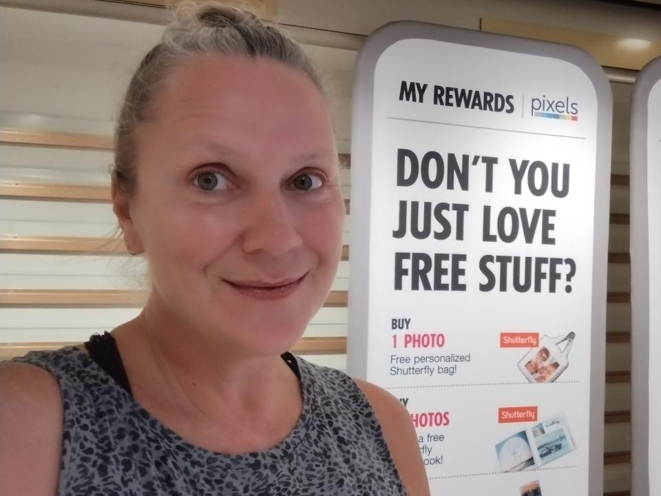 blonde woman posing for a selfie in front of a large, white sign that says "don't you just love free stuff?"