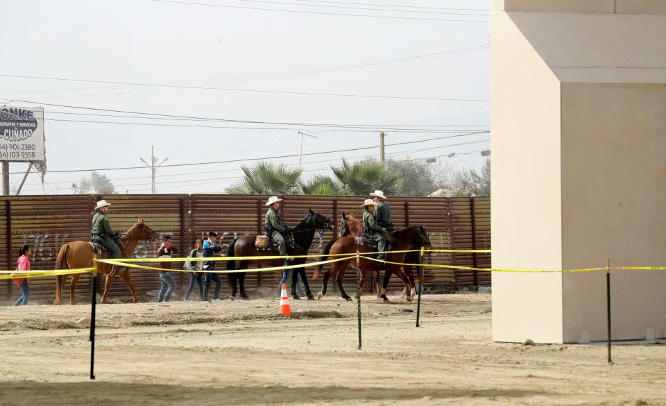 On Oct. 19, 2017, a group of people are detained by Border Patrol agents on horseback after crossing the border illegally from Tijuana, Mexico, near where prototypes for a border wall, right, were being constructed in San Diego.