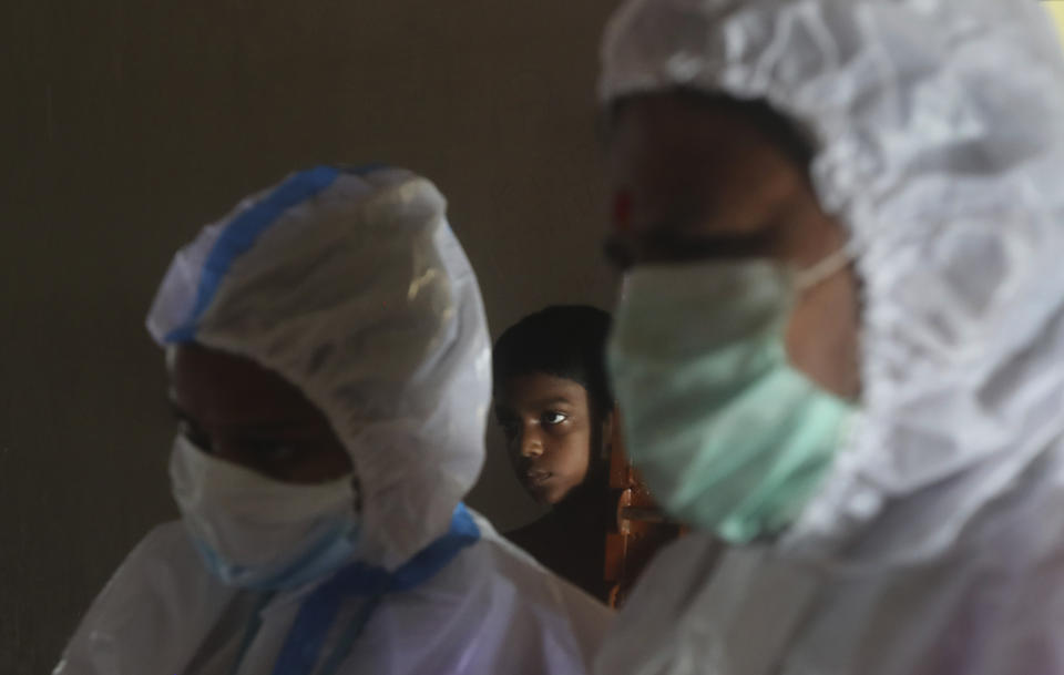 A boy looks on as health workers screen people for COVID-19 symptoms at a residential building in Dharavi, one of Asia's biggest slums, in Mumbai, India, Friday, Aug. 7, 2020. As India hit another grim milestone in the coronavirus pandemic on Friday, crossing 2 million cases and more than 41,000 deaths, community health volunteers went on strike complaining they were ill-equipped to respond to the wave of infection in rural areas. (AP Photo/Rafiq Maqbool)
