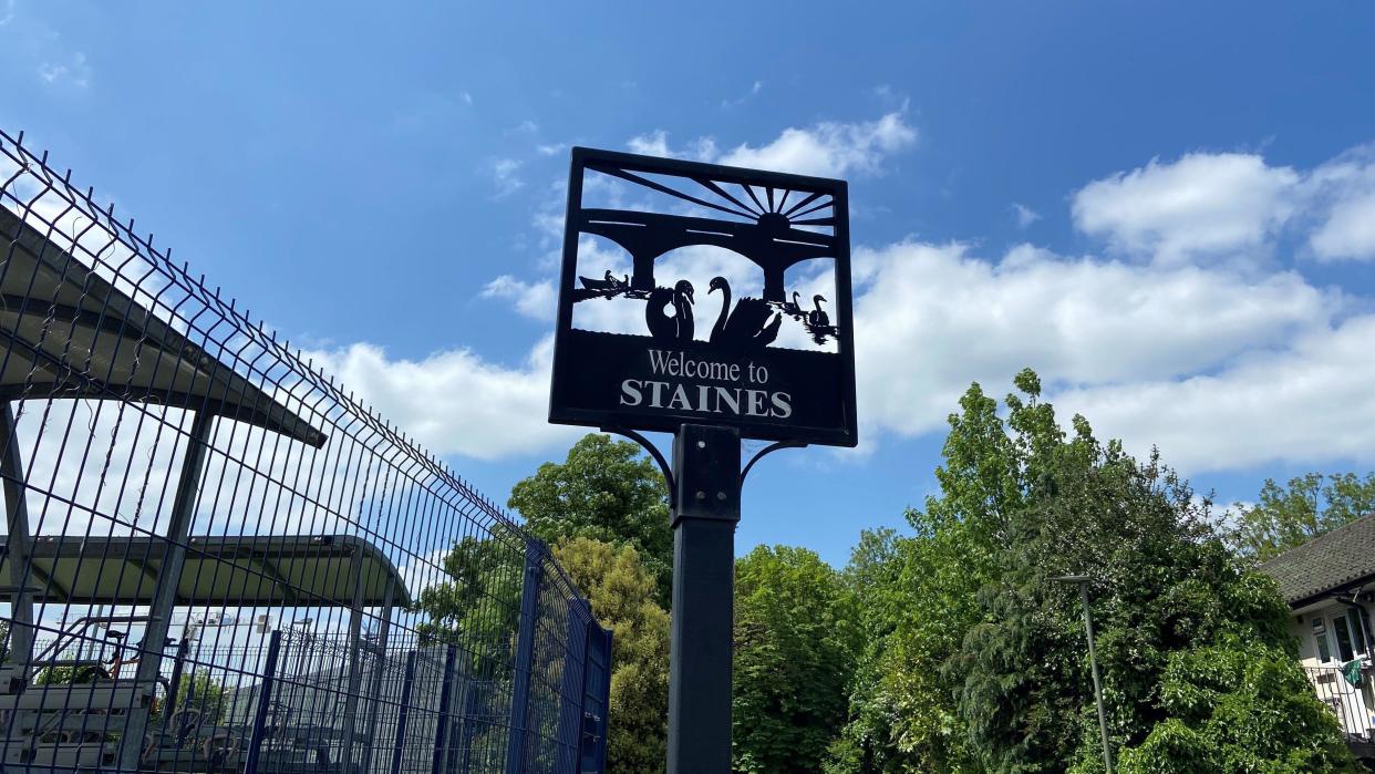 A sign saying welcome to Staines and with swans swimming on a river on it