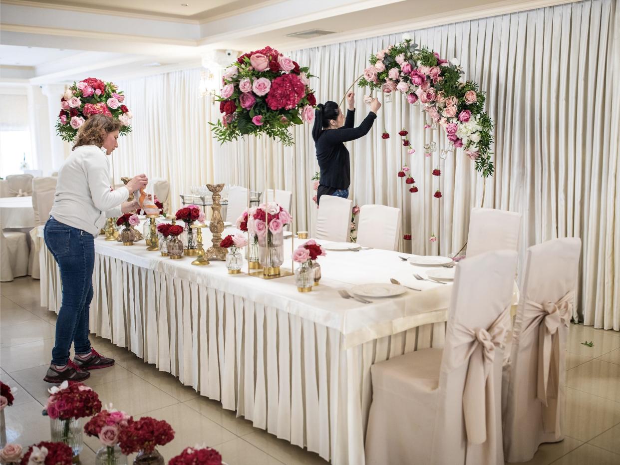 Two wedding vendors setting up room with white table and lots of pink flowers