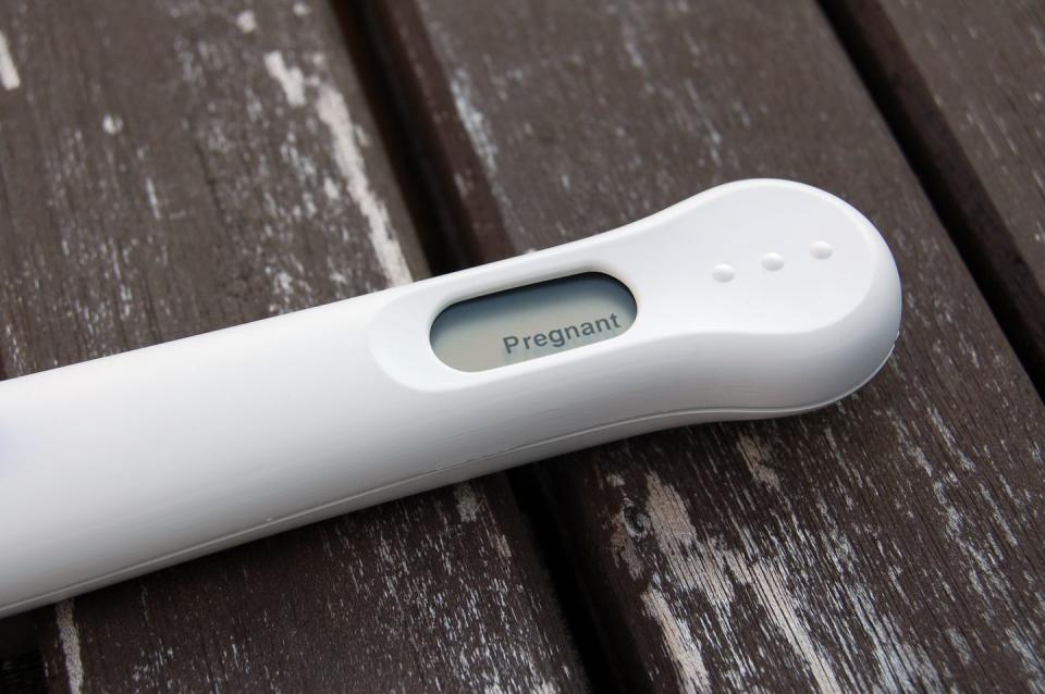 white pregnancy test reading pregnant on a wood surface