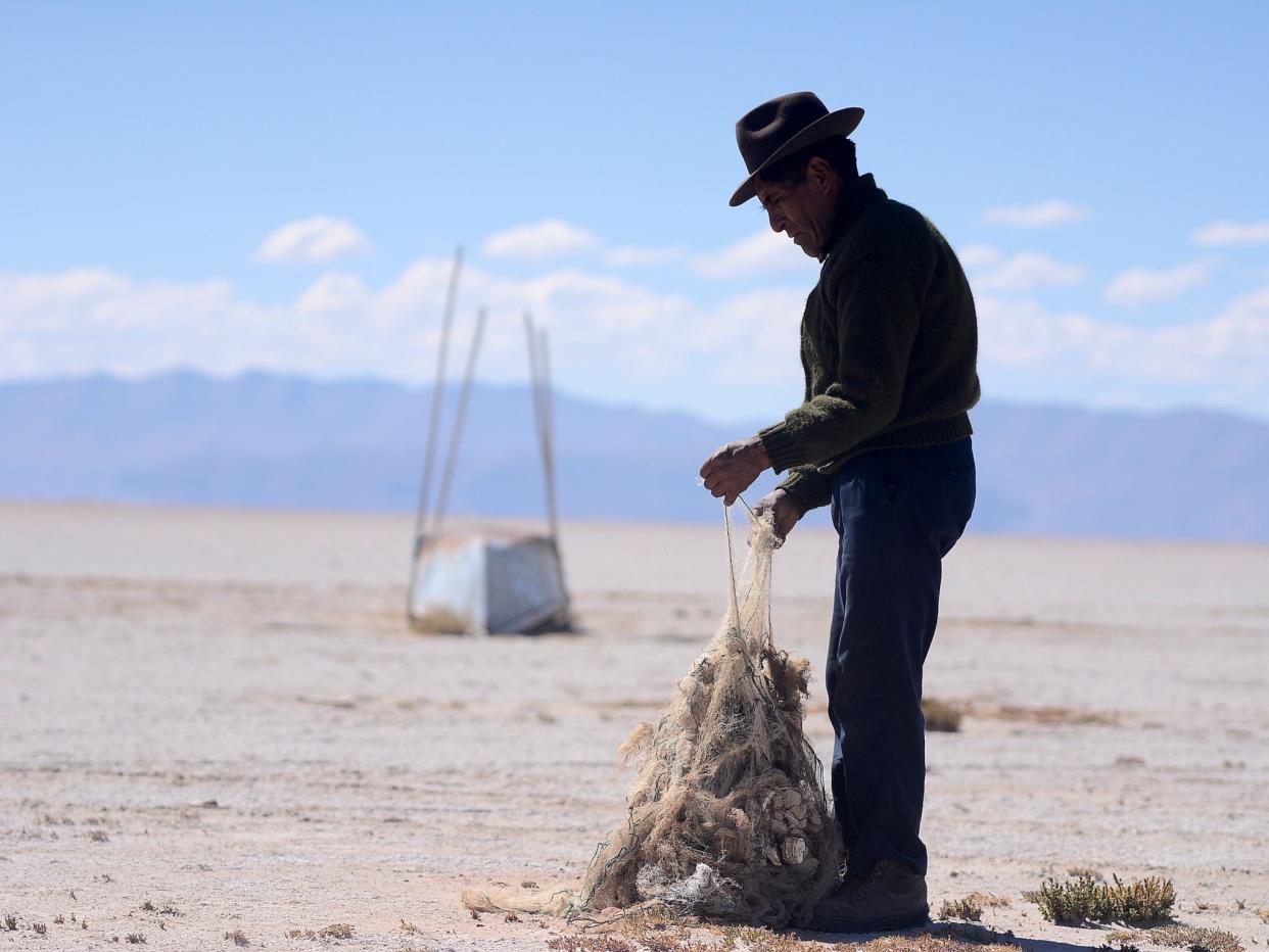 man stands in desert pick apart tangled old fishing net near abandoned boat