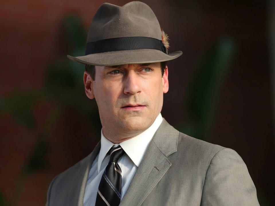 Jon Hamm as Don Draper in a grey suit and fedora