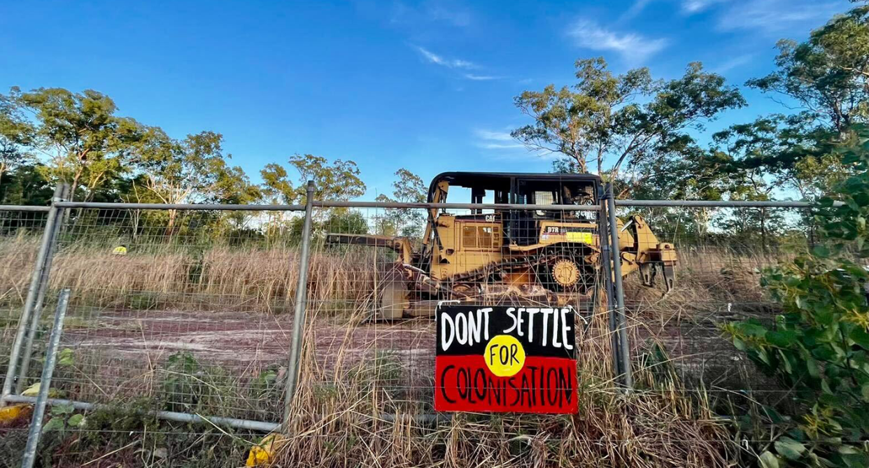 A bulldozer behind a gate at Lee Point. There is an Aboriginal flag poster on the gate.