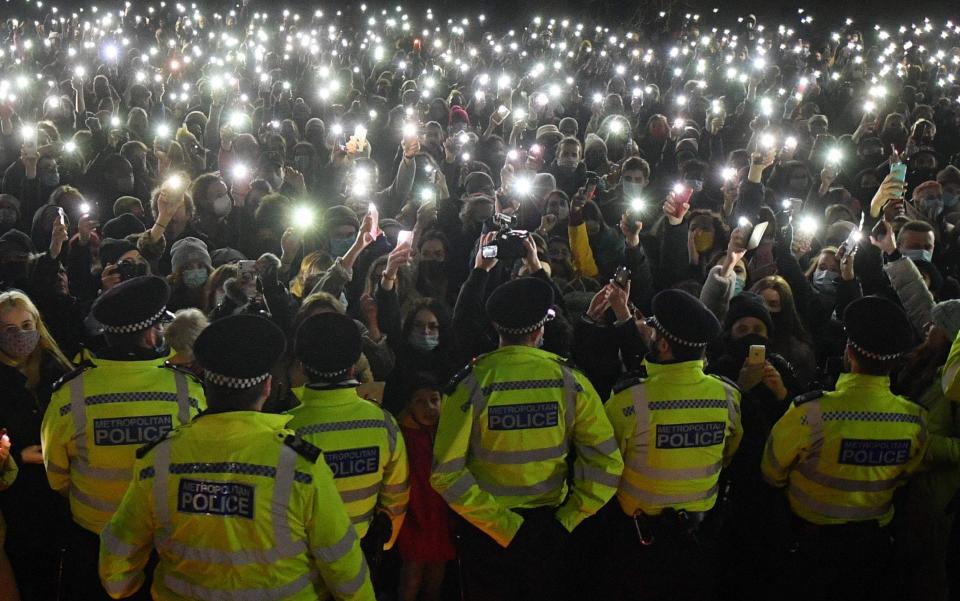 Police officers form a cordon as well-wishers turn on their phone torches as they gather at a band-stand where a planned vigil in honour of murder victim Sarah Everard was cancelled - AFP