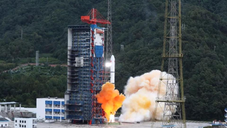 a rocket lifts off from a launch pad with trees behind it