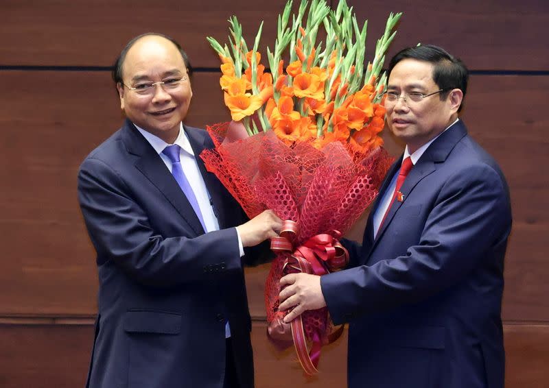 Vietnam's new Prime Minister Pham Minh Chinh holds a bouquet of flowers with country's former Prime Minister Nguyen Xuan Phuc who became the new president, at an official ceremony in Hanoi