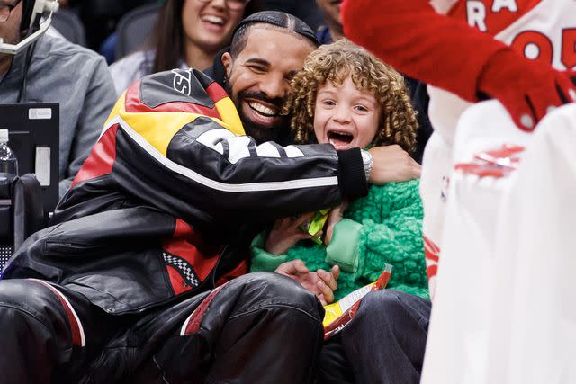 Cole Burston/Getty Images Drake embraces his son Adonis as the Raptor mascot brings over candy for him during the first half of the NBA game between the Toronto Raptors and the LA Clippers at Scotiabank Arena on December 27, 2022 in Toronto, Canada