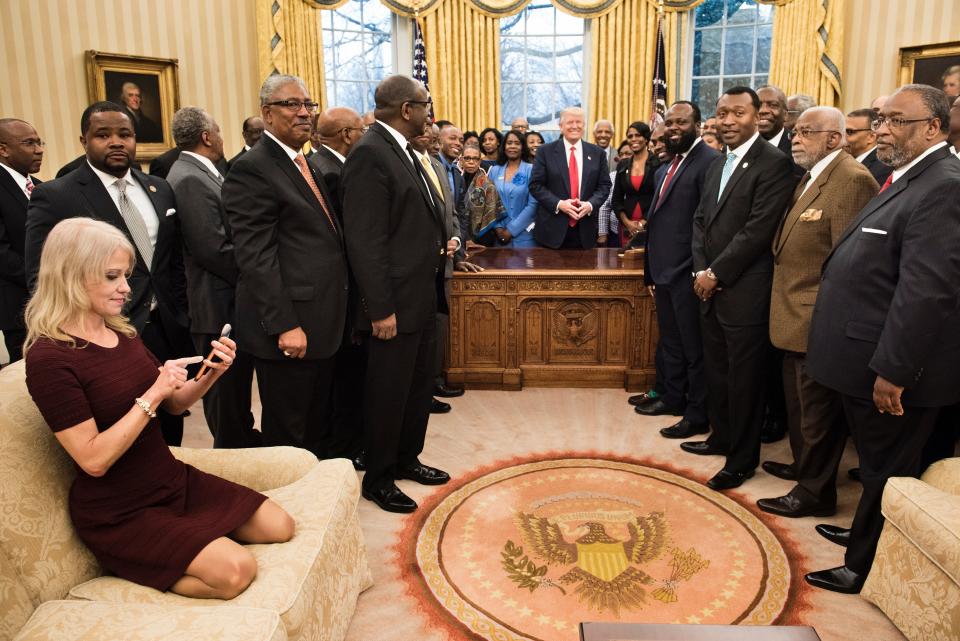 Trump counselor Kellyanne Conway, left, checks her phone after taking a photo as Trump and leaders of historically black universities and colleges pose for a group photo in the Oval Office of the White House before a meeting with Pence on Feb. 27, 2017.