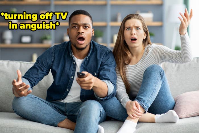 Couple on couch looking upset at what's on TV