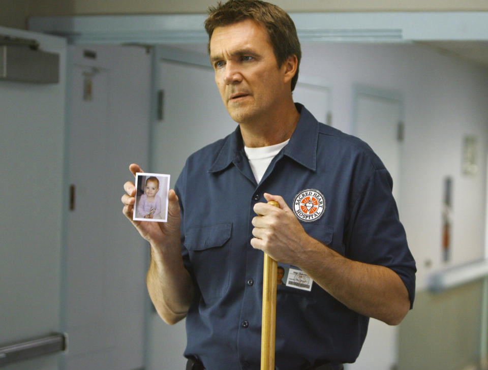 The Janitor holding a broom and a photo of a baby on "Scrubs"