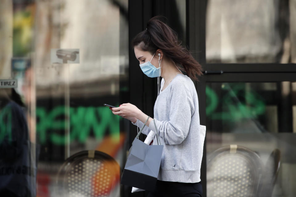 FILE - In this photo taken on April 20, 2020, a woman wearing protective face mask looks at her phone past a closed restaurant during a nationwide confinement to counter the COVID-19, in Paris. French lawmakers are set to vote on whether allowing or not France's contact-tracing app designed to contain the spread of the coronavirus that is raising privacy concerns. (AP Photo/Francois Mori, File)