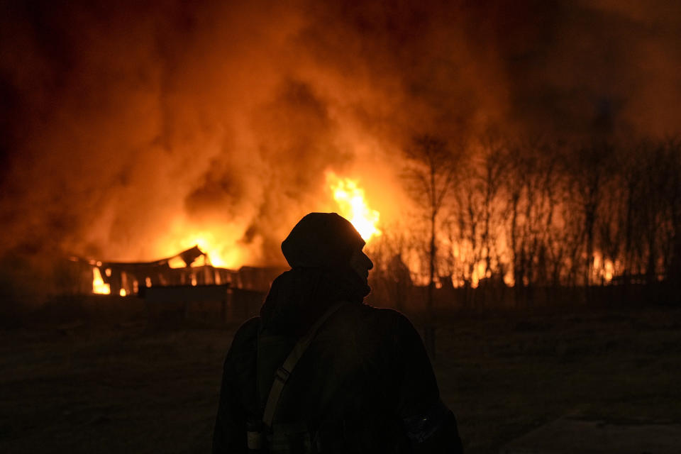 A Ukrainian serviceman is backdropped by a blaze at a warehouse after a bombing on the outskirts of Kyiv, Ukraine, Thursday, March 17, 2022. (AP Photo/Vadim Ghirda)