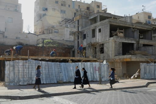 Ultra-orthodox Jews walk in the Israeli settlement of Beitar Illit as Palestinian labourers work at a construction site on February 14, 2018