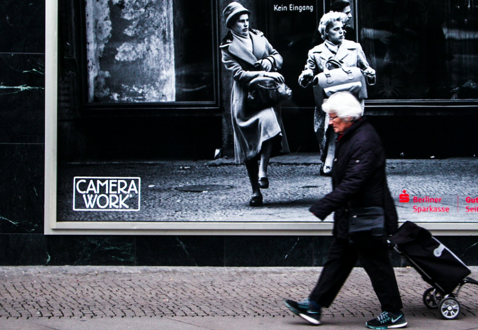 An elderly woman fits in well with an advertising board next to her.