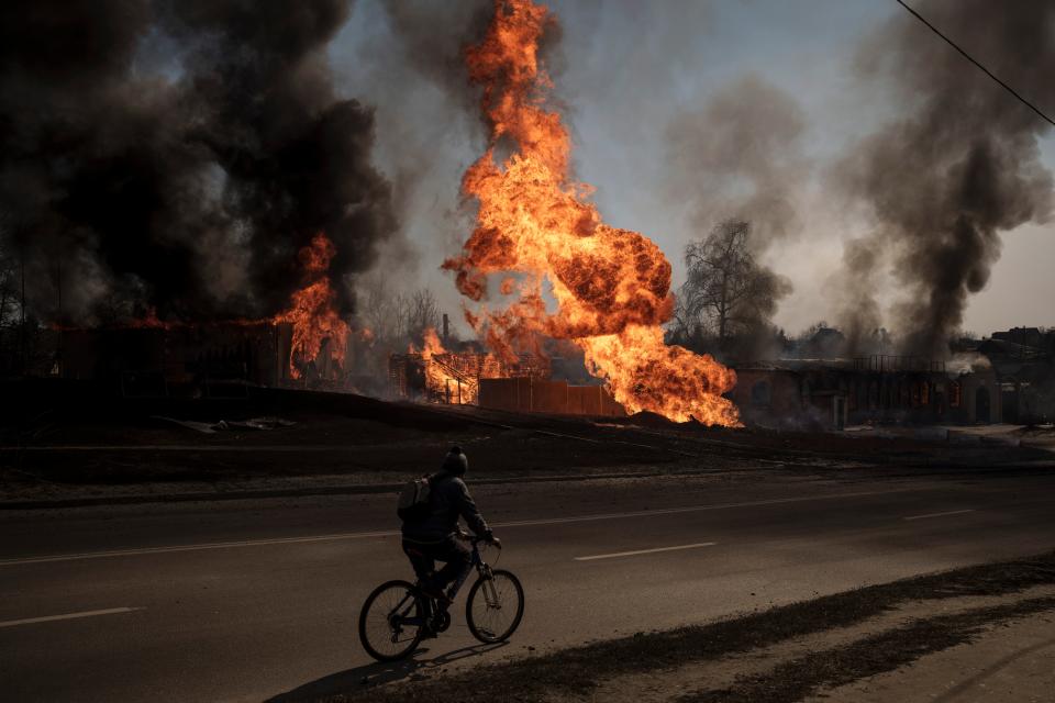 A man cycles past flames after a Russian attack in Kharkiv on 25 March, 2022. (AP)