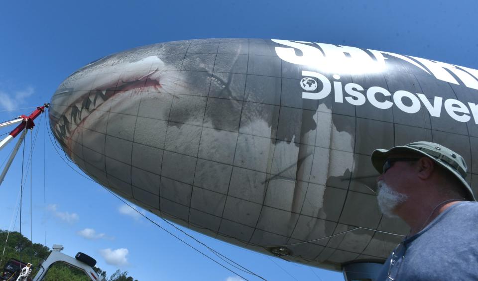 Ground crew member Steve O'Brien keeps an eye on the 130-foot blimp covered in a shark decal on a tour promoting the Discovery Channel's Shark Week at the Cape Cod Airfield in Marstons Mills after arriving there Monday night. The blimp will be flying over Cape beaches on Thursday before heading to its next stop in CT on Friday. Steve Heaslip/Cape Cod Times
