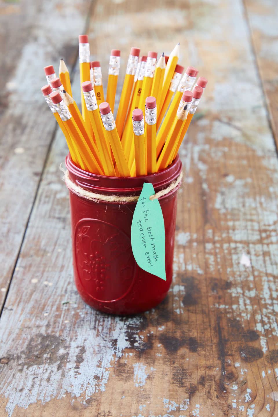 a mason jar painted red with a green leaf gift tag and pencils in the gar