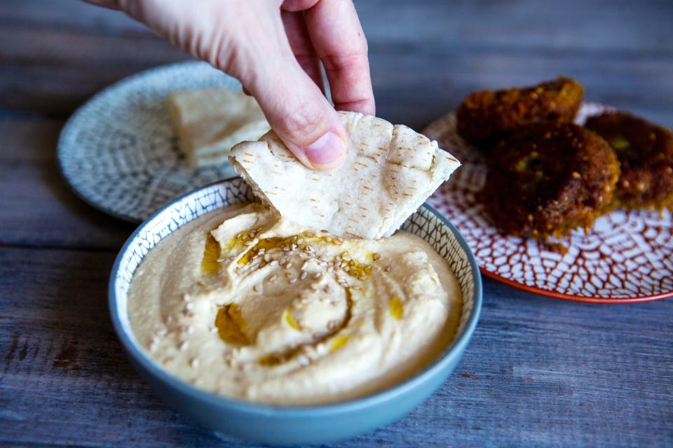 A person dips a piece of pita into a bowl of hummus