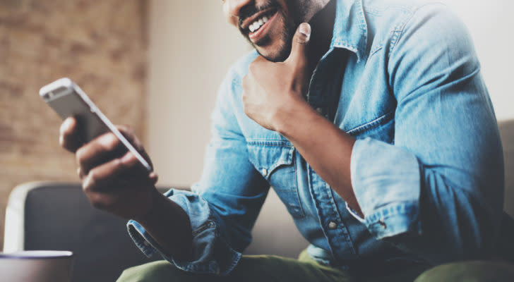 A man sits on his couch looking at his smartphone.