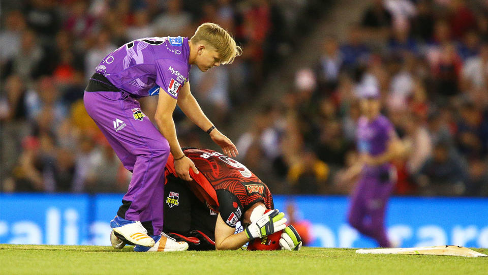 Nathan Ellis checks if Sam Harper is okay as he lies on the floor holding his head.