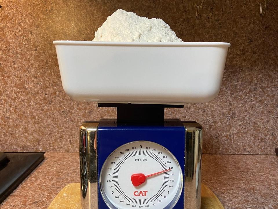 A scale with a dial pointing to 600 grams and tray towering with flour.