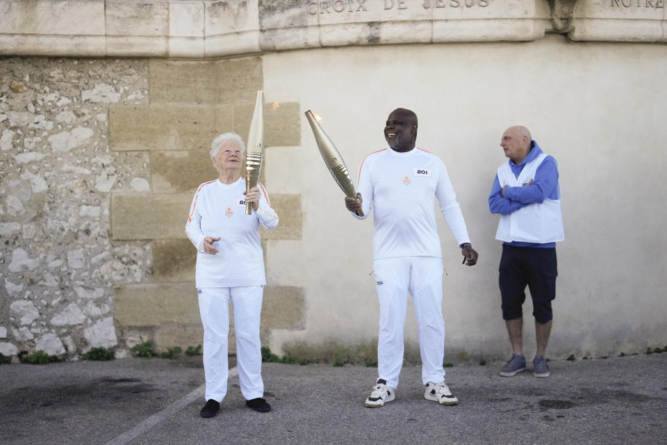 French torchbearers Colette Cataldo, left, and Basile Boli perform a torch kiss during the first stage of the Olympic torch relay in Marseille, southern France, Thursday, May 9, 2024. Torchbearers are to carry the Olympic flame through the streets of France' s southern port city of Marseille, one day after it arrived on a majestic three-mast ship for the welcoming ceremony. (AP Photo/Thibault Camus)