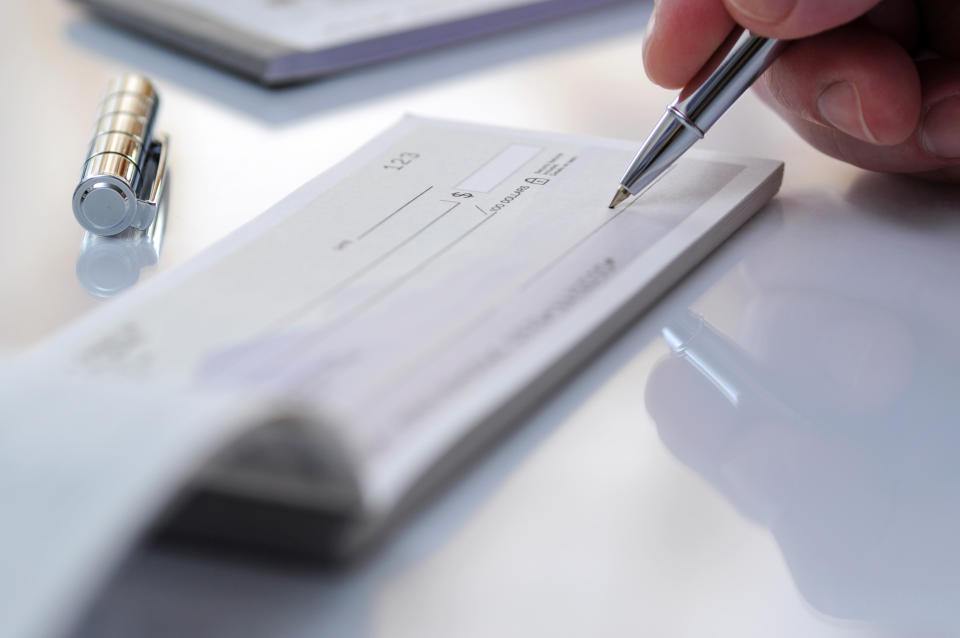 A person is writing a check with a pen on a checkbook. A pen cap rests nearby on the table