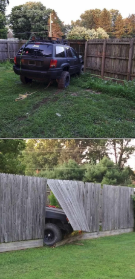 A black SUV crashed through a wooden fence in a grassy backyard. The vehicle appears to be stuck, with damage to the fence and surrounding lawn