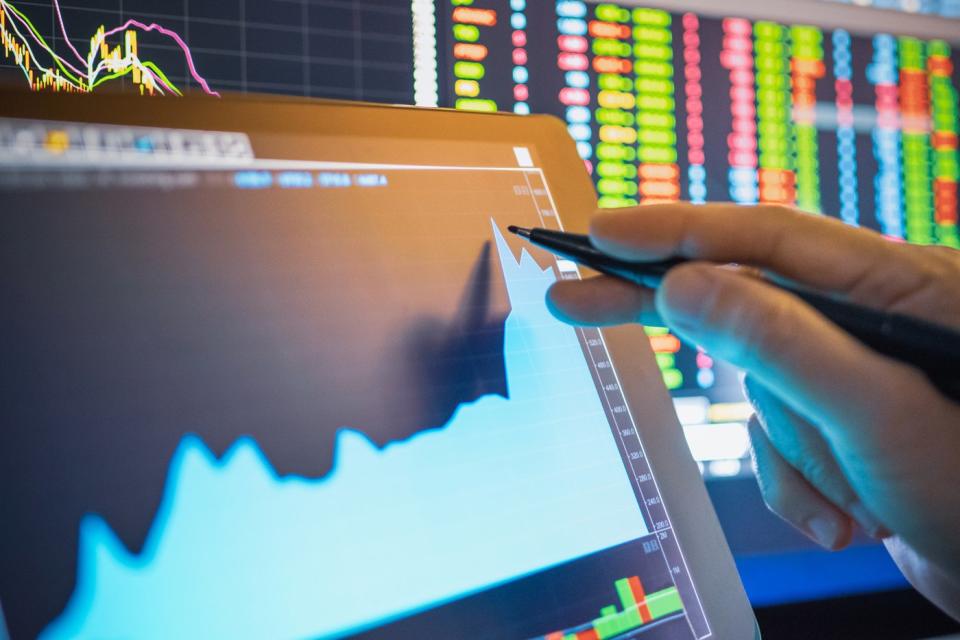 A professional trader using a stylus to interact with a tablet displaying a rapidly rising stock chart.