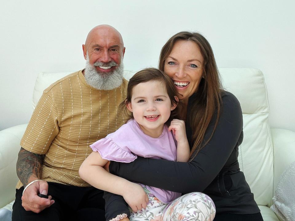 A mother and father with their little girl sitting on a white sofa.