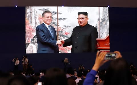 Journalists in the South Korean capital Seoul watch a huge screen showing President Moon Jae-in, left, shake hands with North Korean leader Kim Jong-un - Credit: Lee Jin-man/AP