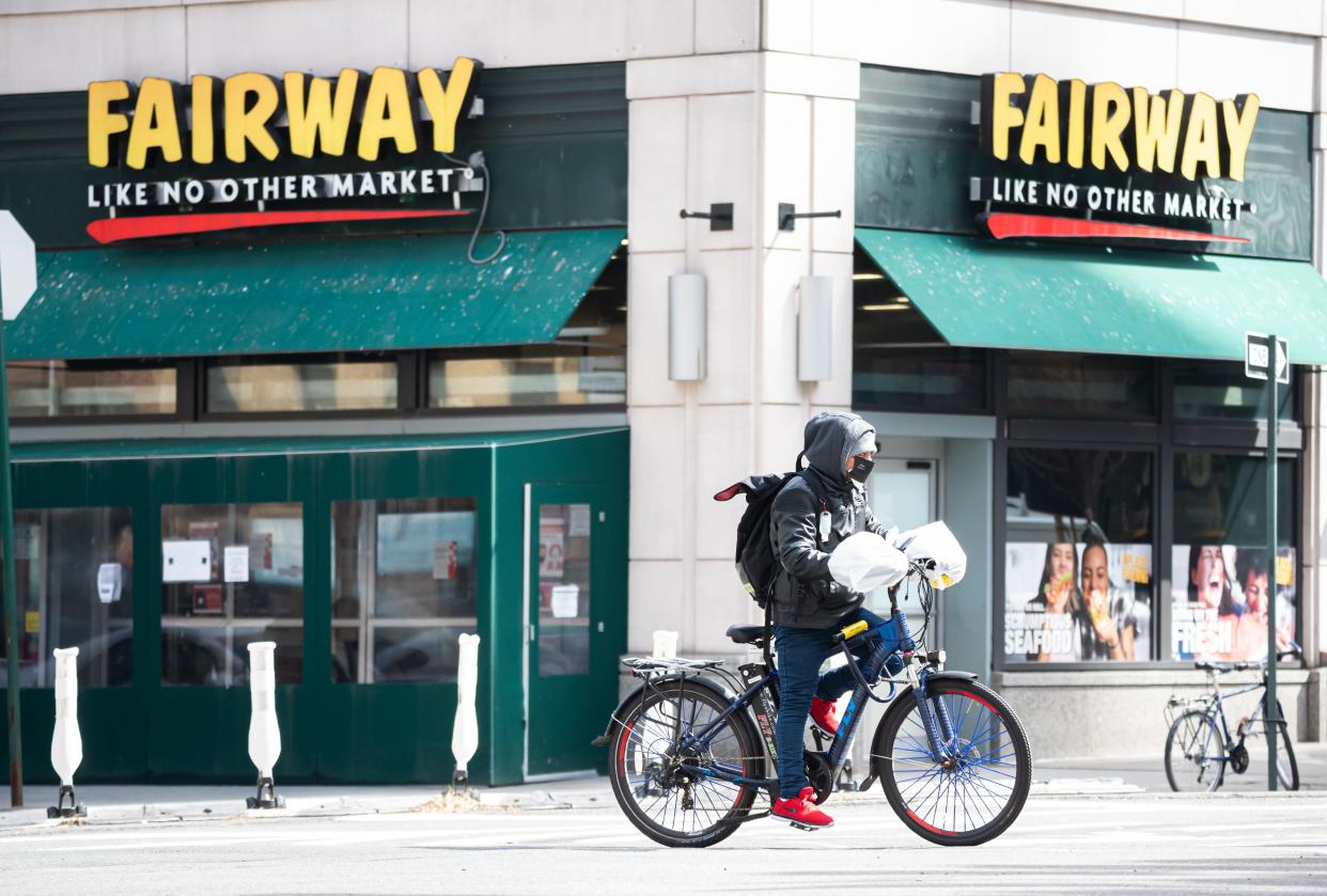 A delivery worker wearing a face mask rides by a Fairway supermarket in Kips Bay in March 2021. The grocer's yellow sign and dark green awnings are visible.