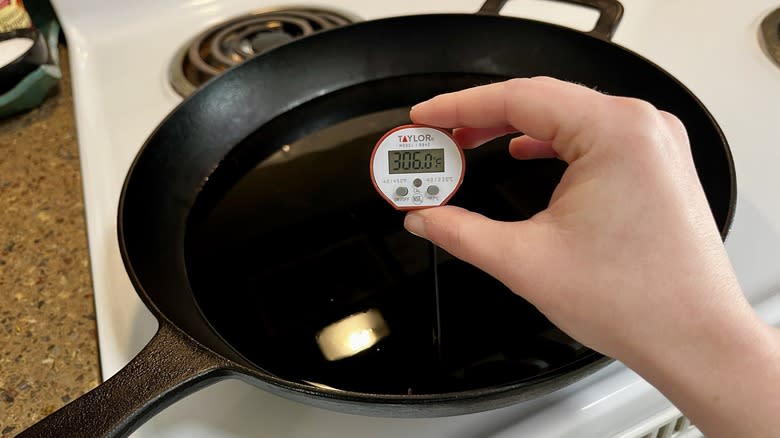 hand holding thermometer over skillet of frying oil
