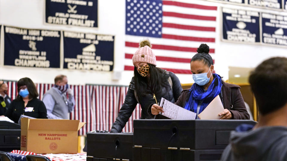 FILE— In this Nov. 3, 2020 file photograph, two women, wearing protective masks due to the COVID-19 virus outbreak, cast their ballots at a polling station at Windham, N.H. High School. Auditors have found no evidence of fraud or political bias in a controversial election in Windham, N.H. (AP Photo/Charles Krupa, File)