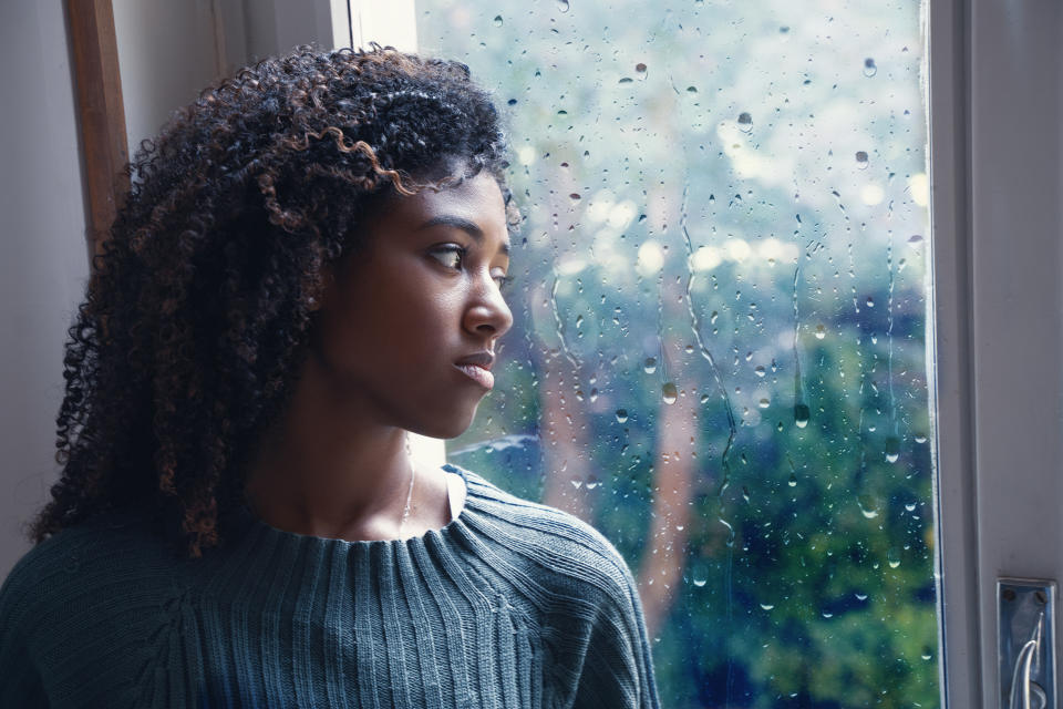 young black woman with curly hair wearing sweater staring out of rain window 