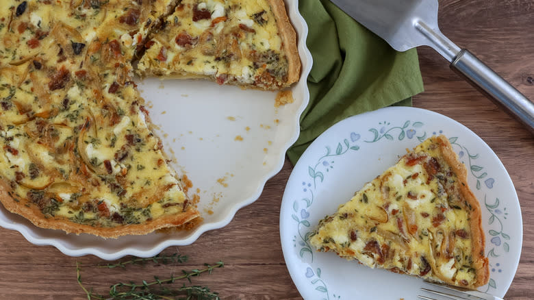 one slice of quiche on a plate with the rest of the quiche in a pan