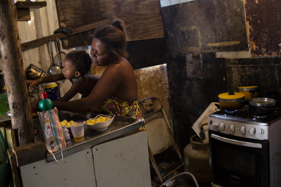 FILE - In this April 18, 2021 file photo, Debora Estanislau, who made her living as a domestic worker before the new coronavirus pandemic hit, holds her one-year-old daughter Ana Beatriz as she cooks at home where she lives with her four children in the Cidade de Deus favela in Rio de Janeiro, Brazil. Limited and reduced welfare payments is leaving vulnerable Brazilians exposed to soaring food prices and a still-worsening job market. (AP Photo/Bruna Prado, File)