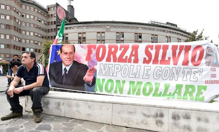 A man sits next to a banner reading "Come on Silvio, Naples is with you, never give up" in front of San Raffaele hospital, as Italian surgeons begin a four-hour heart operation on former prime minister Silvio Berlusconi on Tuesday to replace a defective aortic valve, a hospital statement said, in Milan, Italy June 14, 2016. REUTERS/Flavio Lo Scalzo