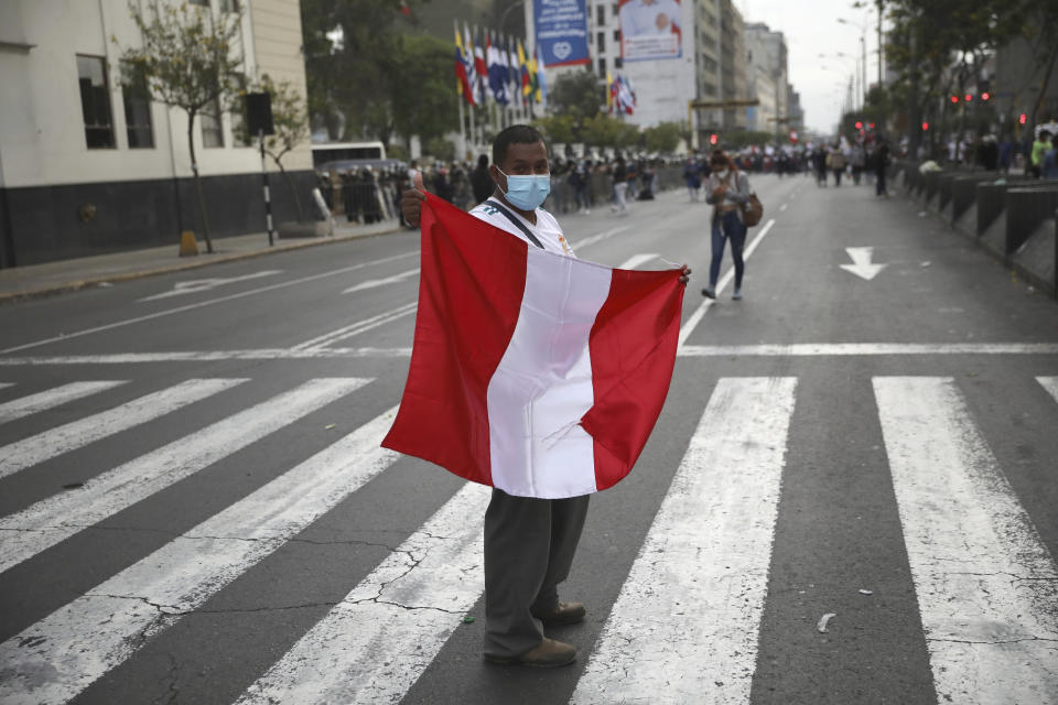 A man holds a Peruvian flag at a street crossing after Peru's new interim President Francisco Sagasti was designated by Congress to lead the nation, in Lima, Peru, Monday, Nov. 16, 2020. Lawmakers chose Sagasti to become the nation's third president in the span of a week after they ousted Martin Vizcarra and the following protests forced his successor Manuel Merino to resign. (AP Photo/Rodrigo Abd)