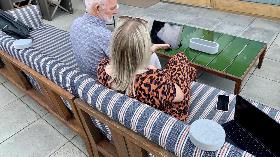 Sony HT-AX7 used on a balcony, in Sound Field mode, being enjoyed by a man and a woman, listening to Harry Stiles on an iPad