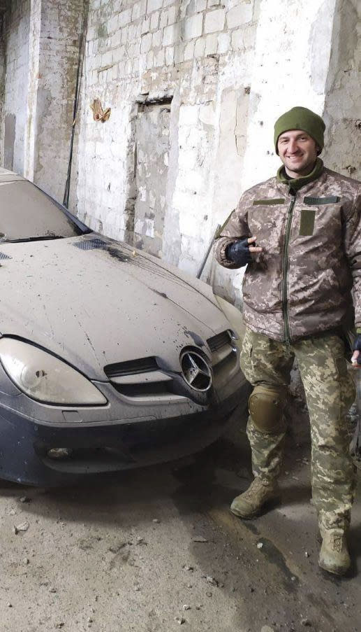 In this photo provided by his family, Oleksandr “Sasha” Romanovych Hrysiuk, in uniform, poses next to a luxury automobile in Ukraine. Soldiers from Sasha's unit said they were very sorry they couldn't take his body with them, the shelling was too heavy, all they could do was hide him in a cellar in Dovhenke – a rural settlement in eastern Ukraine that fell to the Russians. (Courtesy Olha Hrysiuk via AP)