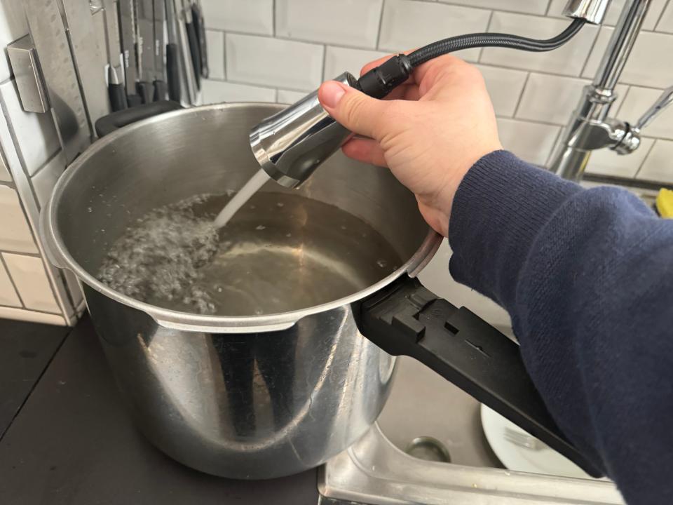 hand filling up a metal pot with water from a kitchen tap